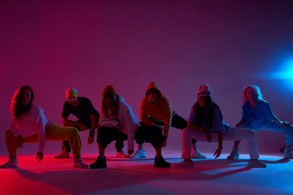 Big group of young people sitting on squat on dark lighted stage, waiting for beginning of music, ready to start dancing, hip hop, street dance, break dancers