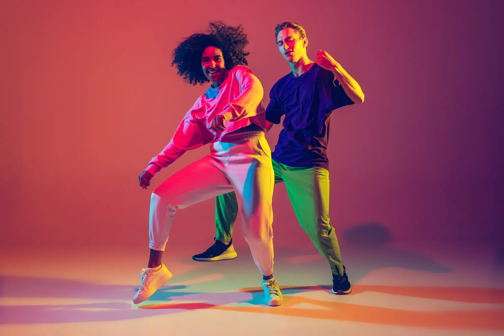 Stylish men and woman dancing hip-hop in bright clothes on gradient background at dance hall in neon light