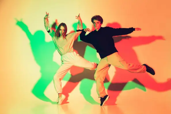 Young beautiful man and woman dancing hip-hop, street style isolated on studio background in neon light
